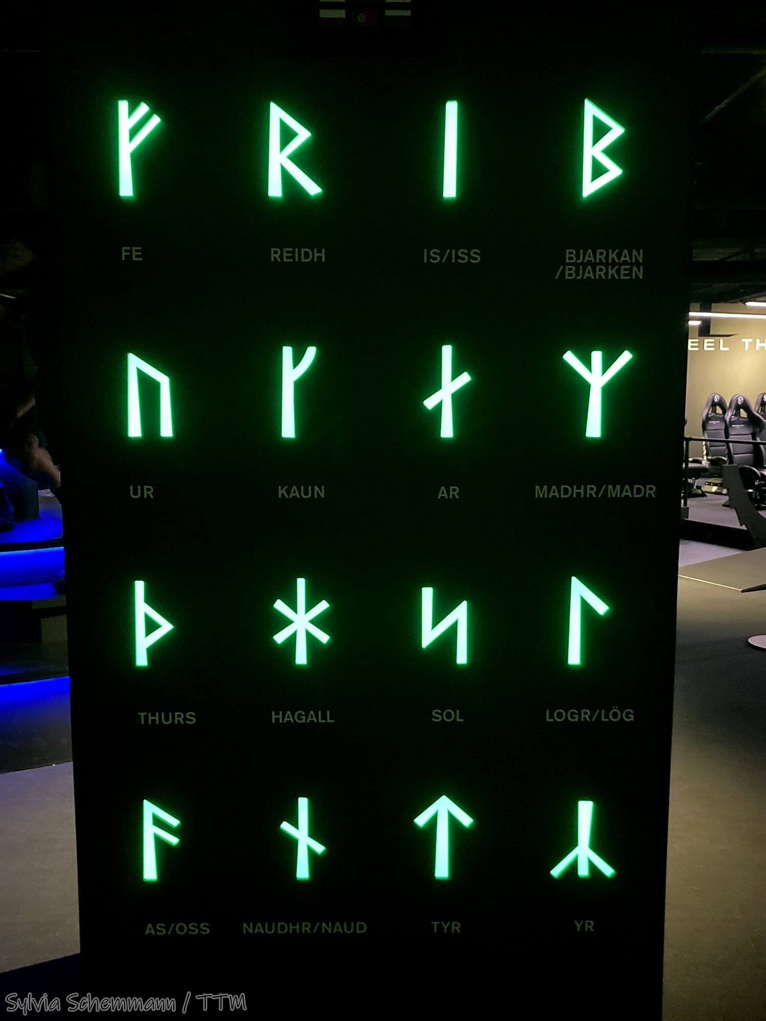 Eine schwarze Tafel, auf der in grüner Leuchtschrift Runen zu sehen sind.