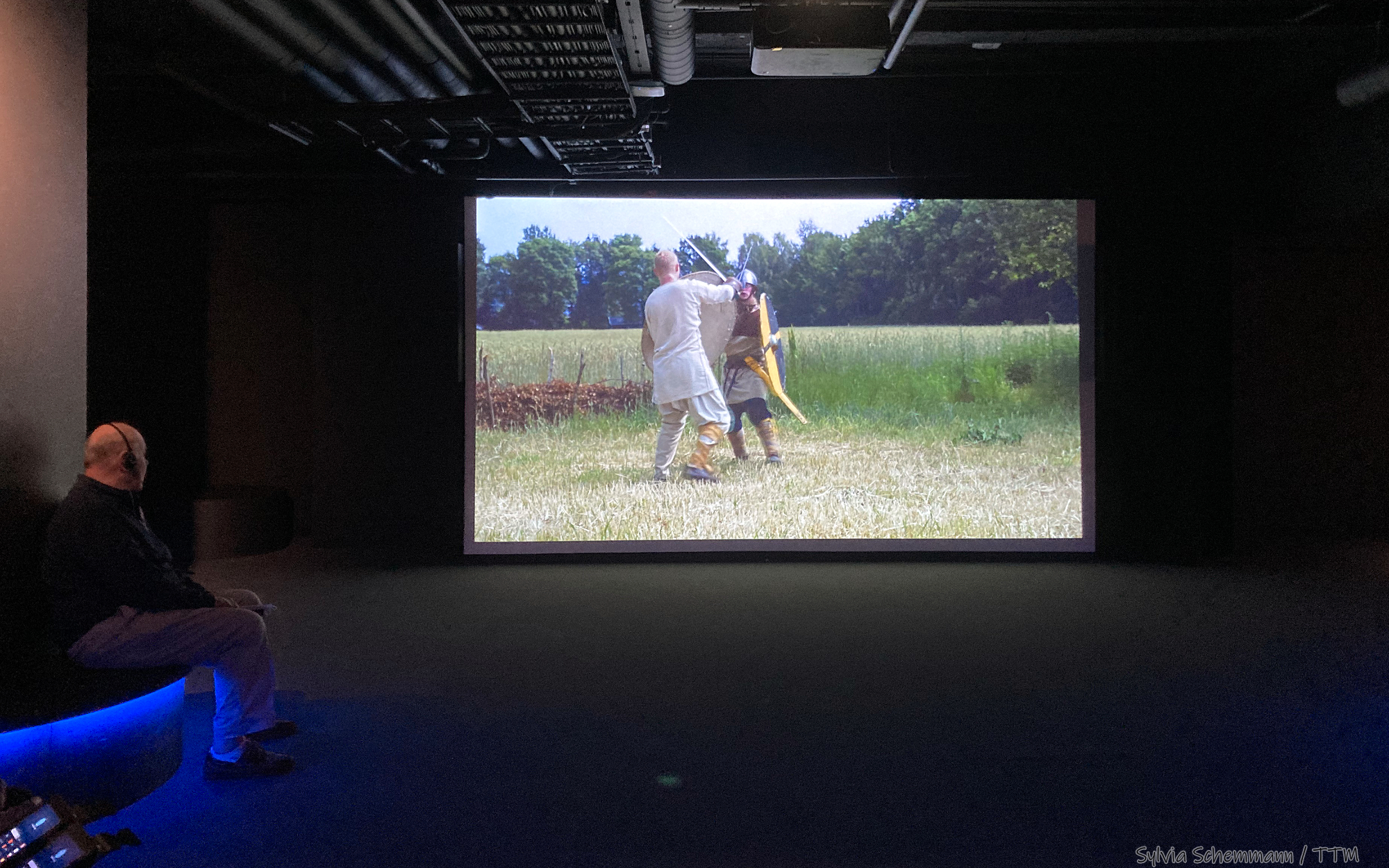 Blick auf eine Leinwand, auf der  in einem Film über die Wikinger in Norwegen zwei kämpfende Krieger zu sehen sind.