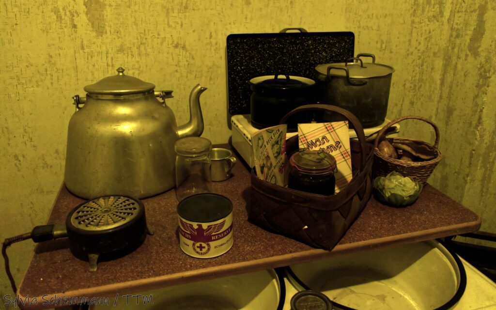 Ein Tisch mit zwei Emaille-Waschschüsseln und einigen historischen Küchenutensilien aus dem Zweiten Weltkrieg und einigen Lebensmitteln - die Küche im Bunker.