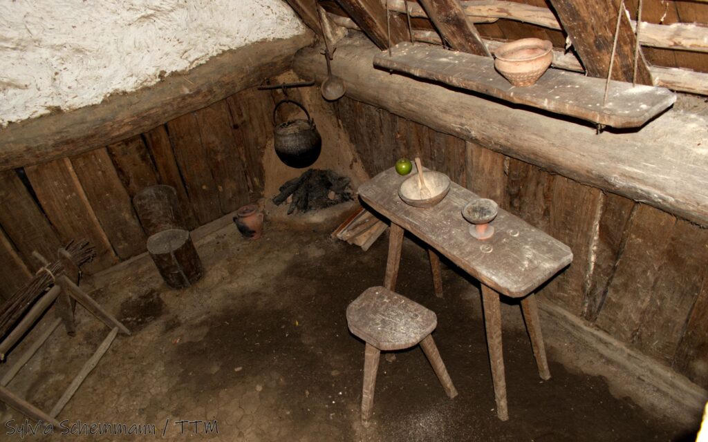 Ein Hocker und ein schmaler Tisch in einem Grubenhaus im Archäologischen Freilichtmuseum Oerlinghausen