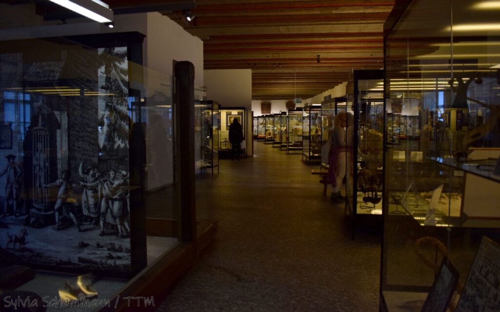 Blick in einen Ausstellungsraum des Mittelalterlichen Kriminalmuseums Rothenburg, auf der rechten Seite stehen viele Vitrinen hintereinander.