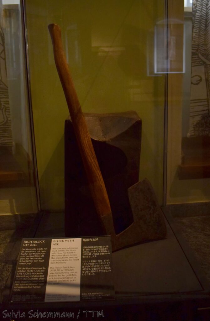 Ein Richtblock, vor dem ein Henkersbeil steht, in einer Vitrine im Kriminalmuseum Rothenburg