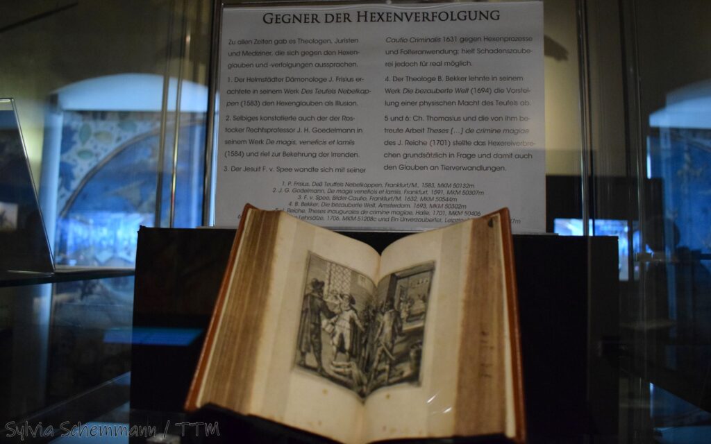 Ein aufgeklapptes, aufgestelltes Buch mit einem Holzschnitt, dahinter eine Schrifttafel mit der Überschrift "Gegner der Hexenverfolgung" im Mittelalterlichen Kriminalmuseum Rothenburg.