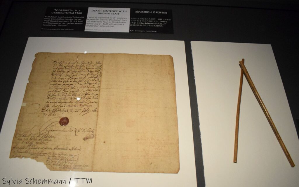 Eine Urkunde über ein Todesurteil aus dem 17. Jahrhundert mit Siegel, daneben ein zerbrochener hölzerner Stab.