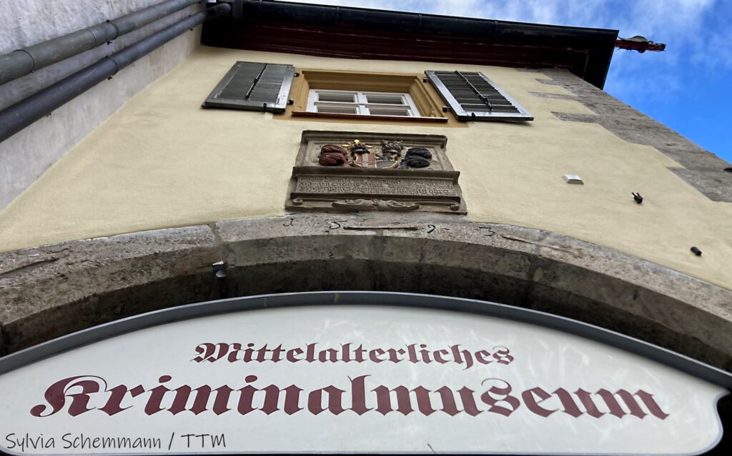 Schild mit der Aufschrift "Mittelalterliches Kriminalmuseum" an einer Häuserfassade, von unten fotografiert.