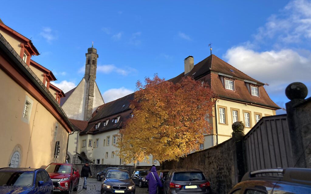 Blick auf das historische Haus des Kriminalmuseums Rothenburg mit hellgelber Fassade, davor ein herbstlich gefärbter Baum.