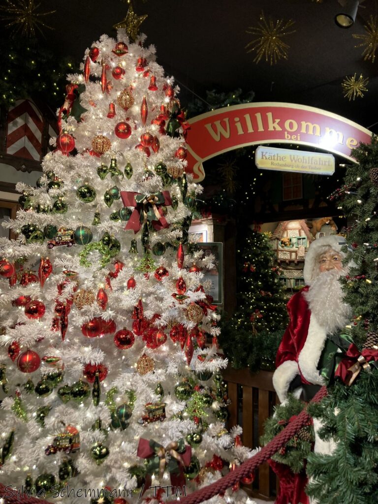 Ein weißer Weihnachtsbaum, daneben ein Nikolaus und ein Schild "Willkommen bei Käthe Wohlfahrt".