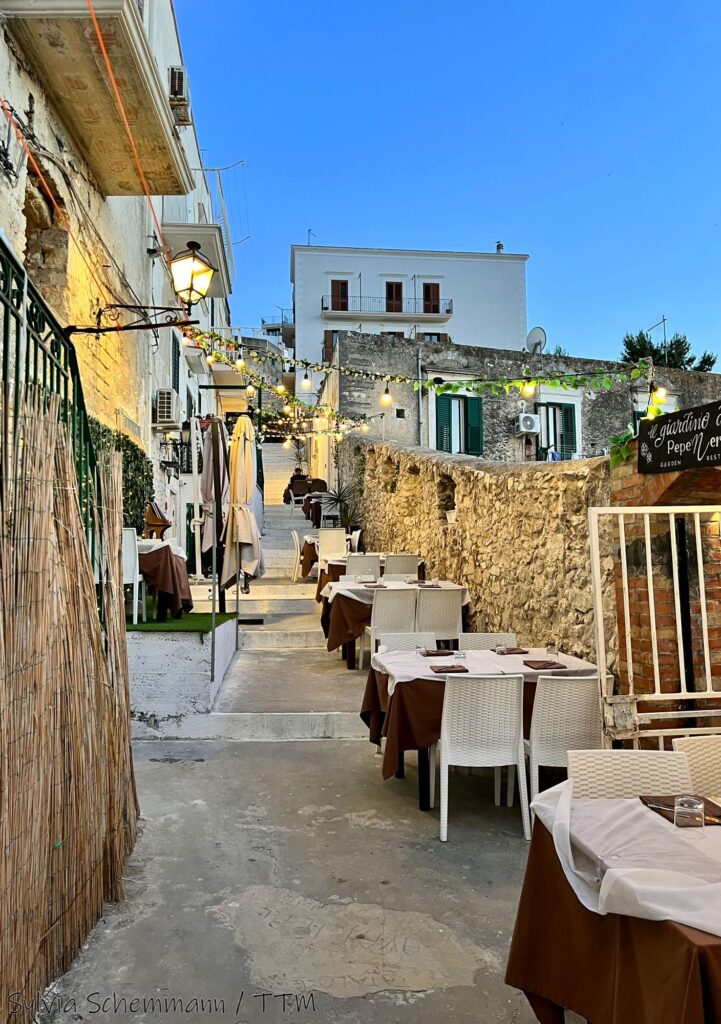 Blick auf Restauranttische an der alten Stadtmauer von Vieste zur blauen Stunde