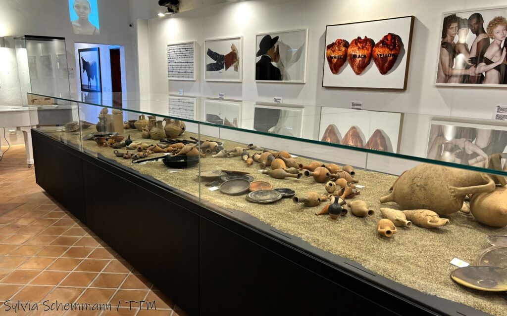 Vitrine mit antiken Amphoren im Museo Archeologico M. Petrone in Vieste, an der Wand dahinter Fotografien