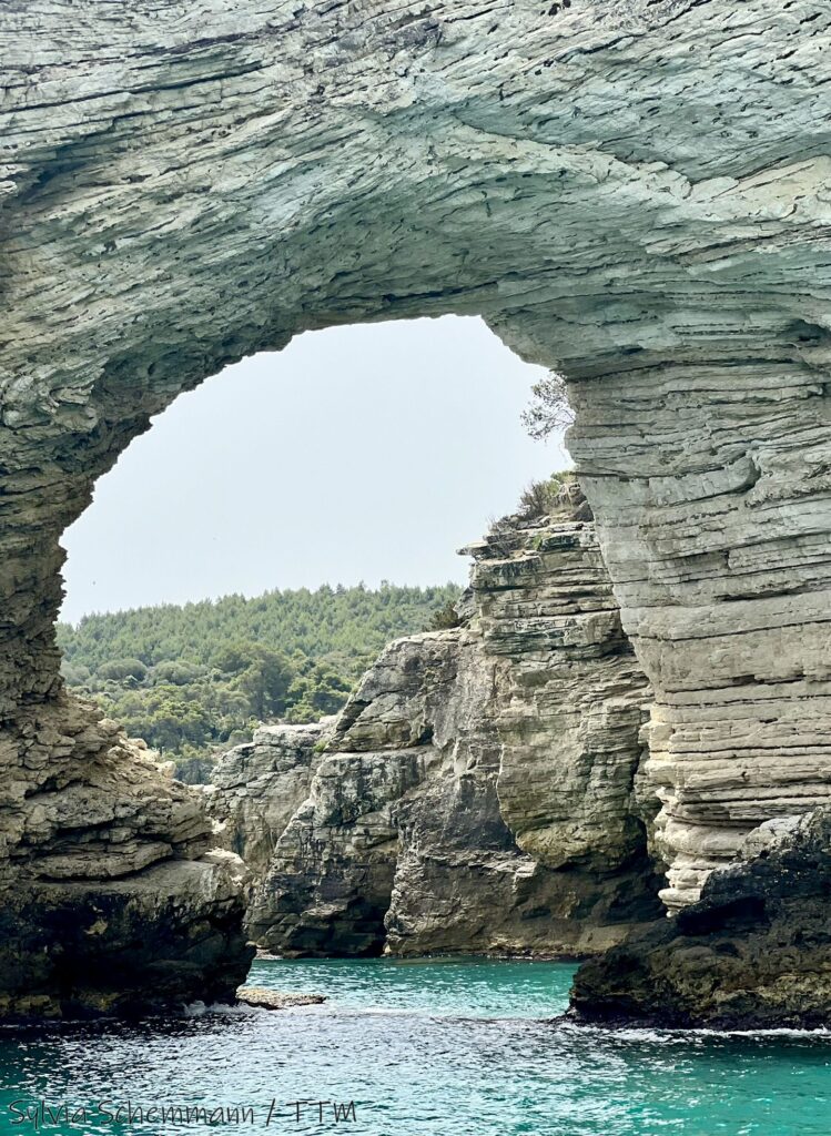 Eine ringförmige Kalksteinformation im Meer, dahinter sind weitere schroffe Kalksteinfelsen erkennbar.