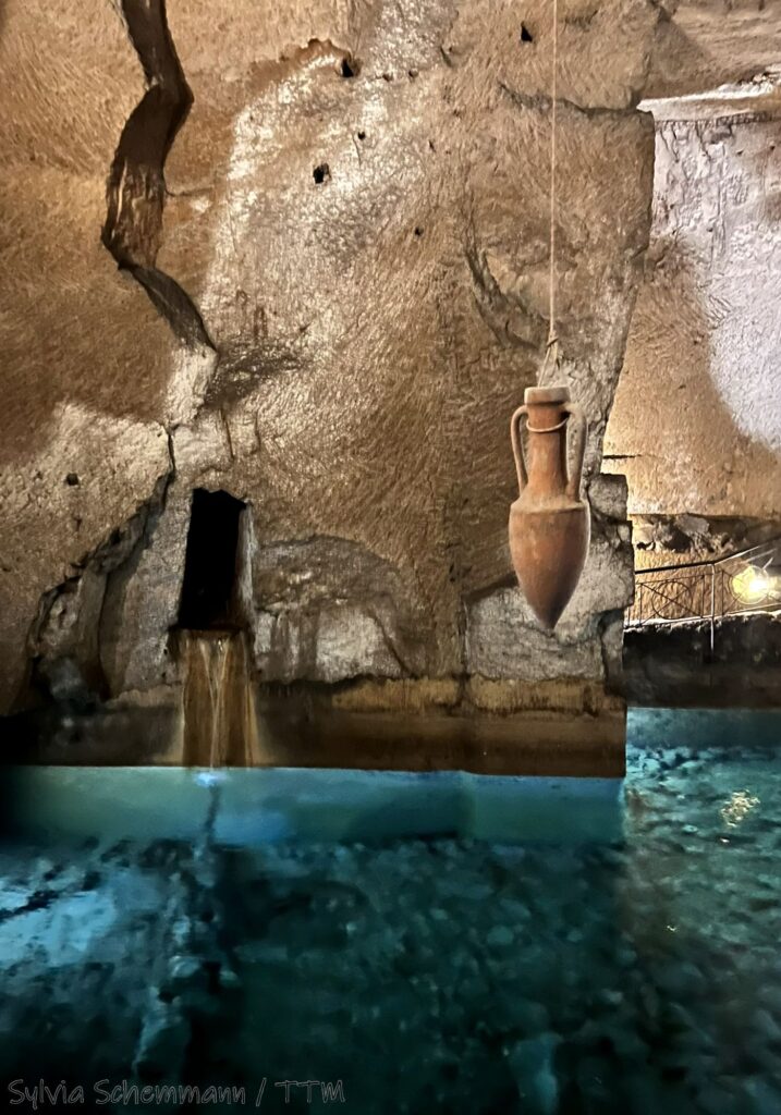 Ein größeres Wasserbecken, darüber hängt eine Amphore an einem Seil